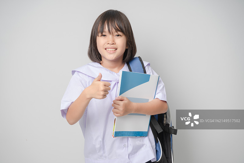 穿校服的女孩拿着一个包，抱着一本书，竖起大拇指图片素材