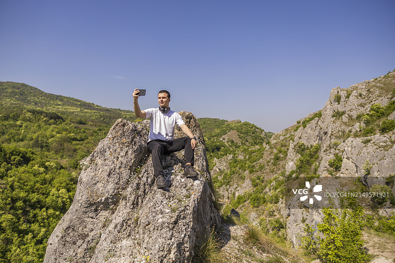 年轻男人坐在山上的岩石上自拍图片素材