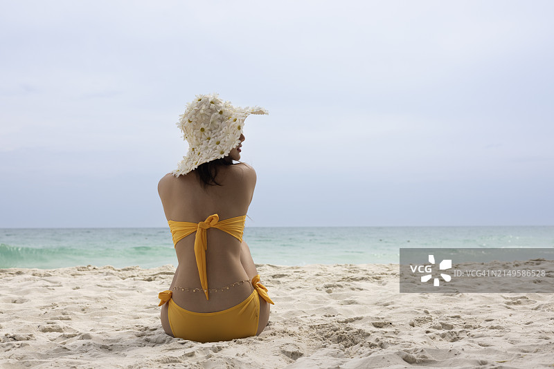 热带海滩上身穿橙色比基尼享受日光浴的美丽女人，快乐的夏季旅行图片素材