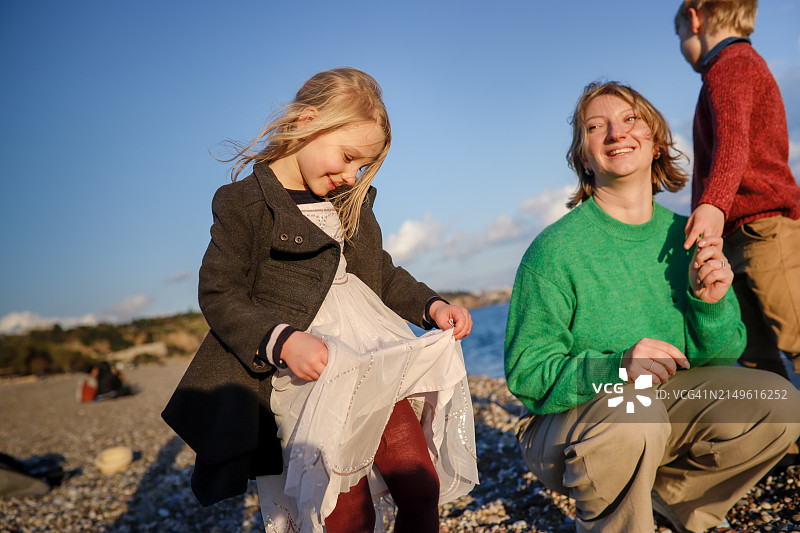 温馨家庭时刻：母亲和两个穿着毛衣的孩子在海边漫步图片素材