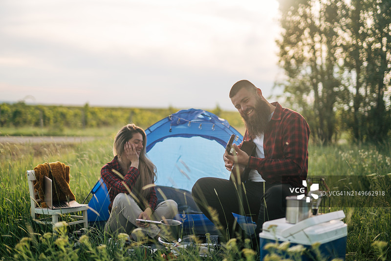 年轻夫妇在野外露营，男人弹吉他，他们一起享受图片素材