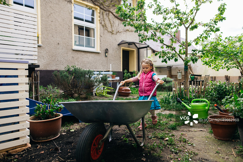 小女孩在家试图推动大号手推车图片素材