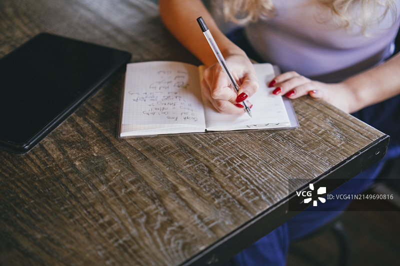 年轻女人在咖啡馆的桌子旁在日记中写笔记图片素材
