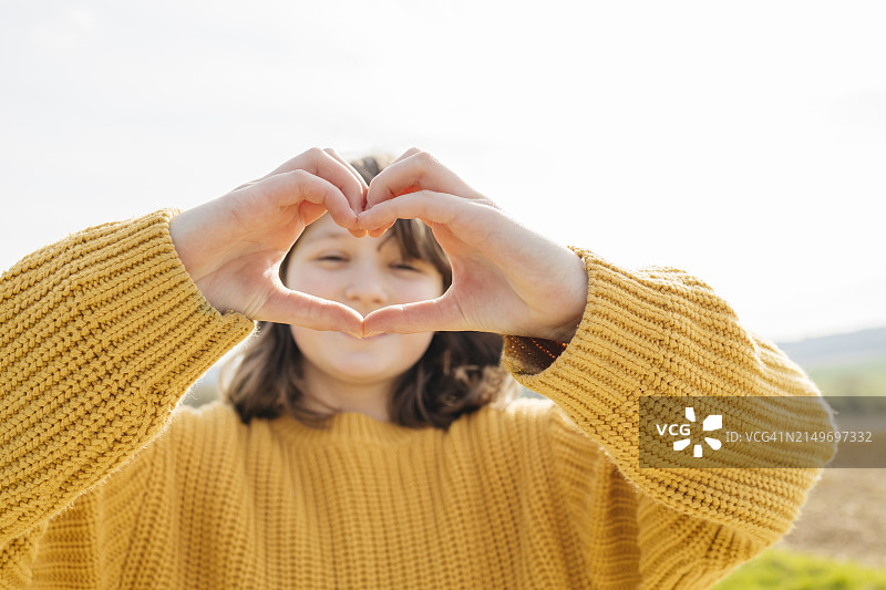 穿黄色毛衣的女孩做心形手势图片素材