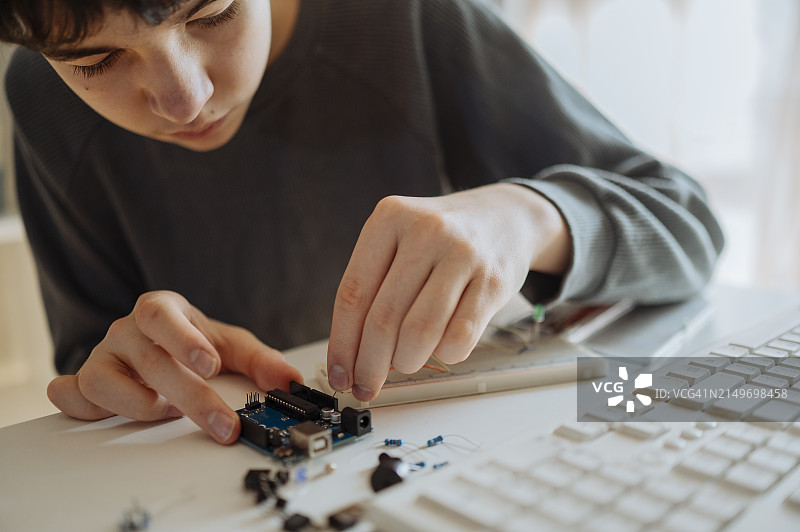 在家中，青少年男孩正在键盘旁调整电子元件图片素材