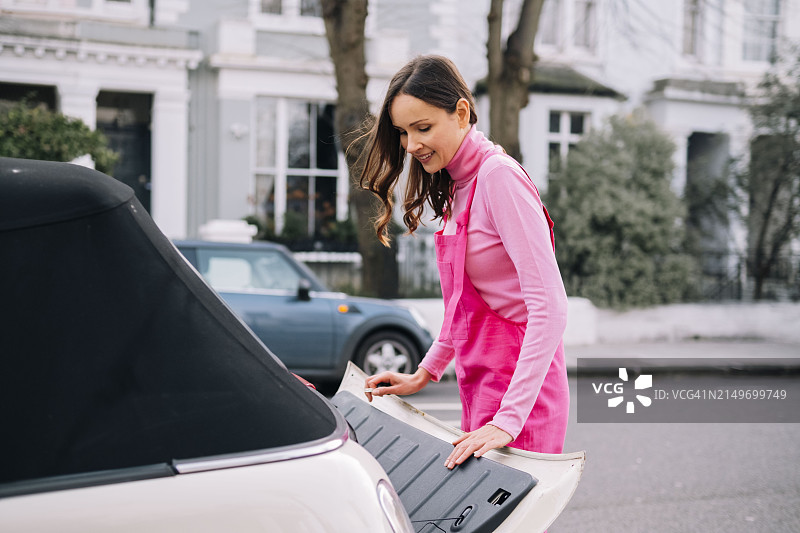 身穿粉色工装裤，在街上打开汽车后备箱的女人图片素材