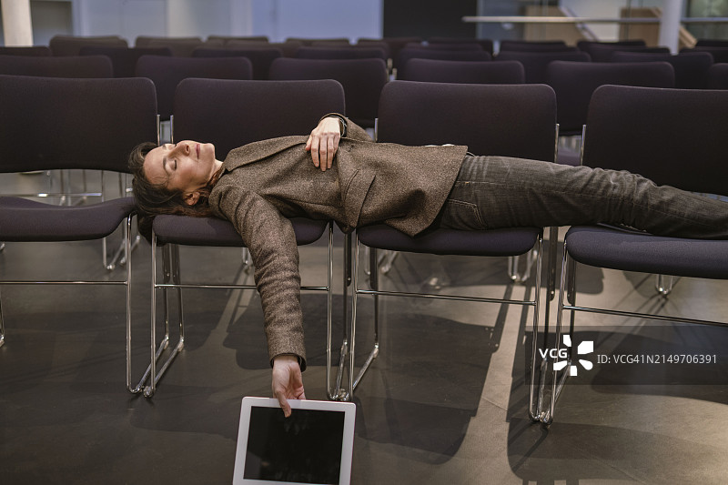 疲惫的教授在讲堂里抱着平板电脑在椅子上睡觉图片素材