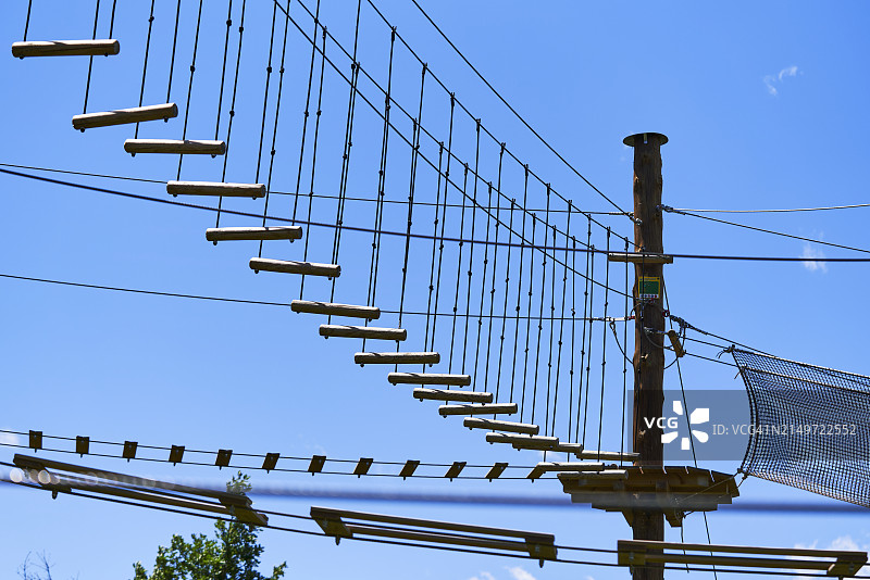 低角度视角：无人的木制吊桥与高空滑索，天空为背景图片素材
