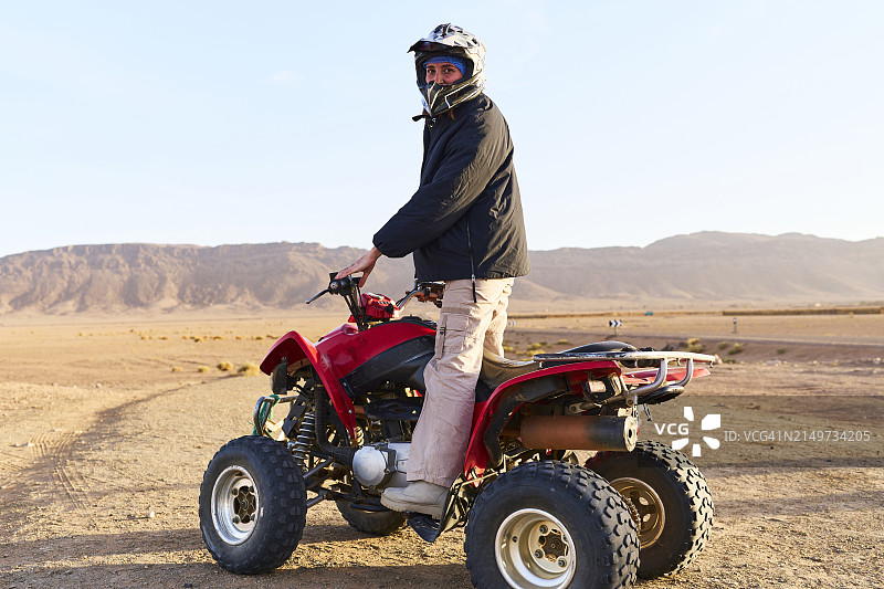 戴头盔的女子在摩洛哥沙漠中骑四轮摩托车侧面照图片素材