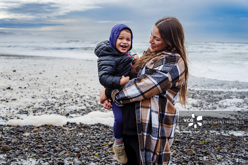 母亲抱着蹒跚学步的儿子站在岩石岸边图片素材