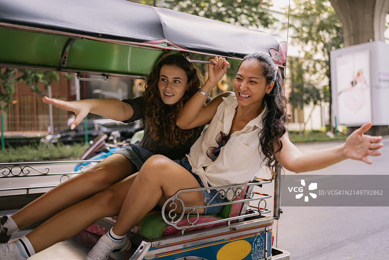 年轻快乐的女人在城市街道上乘坐嘟嘟车时玩得很开心。图片素材