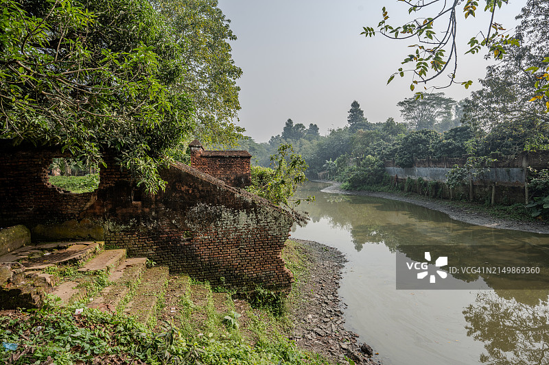 达卡索纳冈宁静水道旁的旧砖建筑，反映了该地区丰富的历史，并以悬垂的树枝为框架图片素材