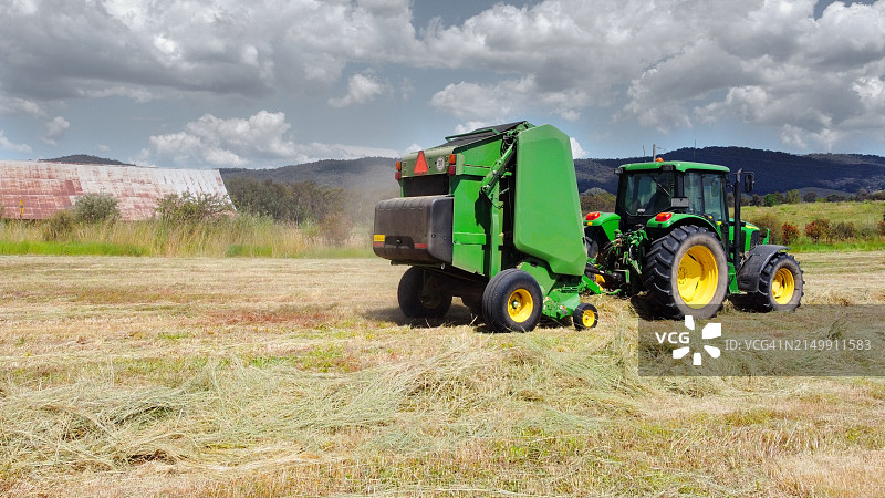 绿色拖拉机牵引绿色农具，准备用于圆形干草捆的稻草图片素材