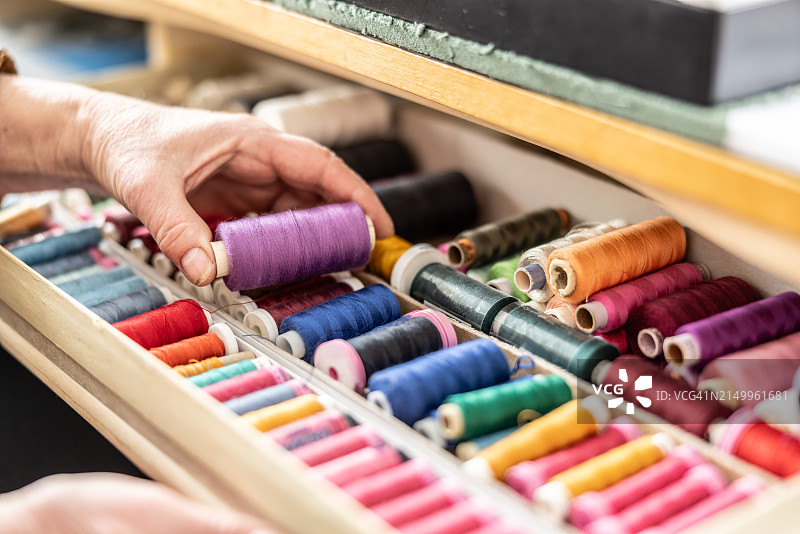 女裁缝的手拿起一卷紫色线，在裁缝工作坊里选择缝纫用彩色线图片素材