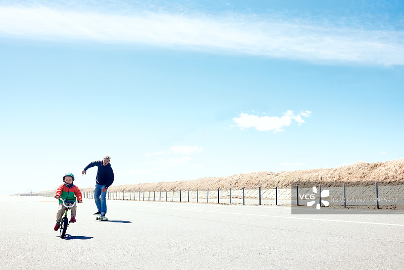 父亲骑自行车追逐玩滑板的儿子图片素材