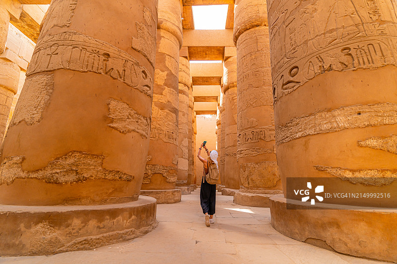 女游客走在卡纳克神庙大柱厅的柱子间，用智能手机拍照图片素材
