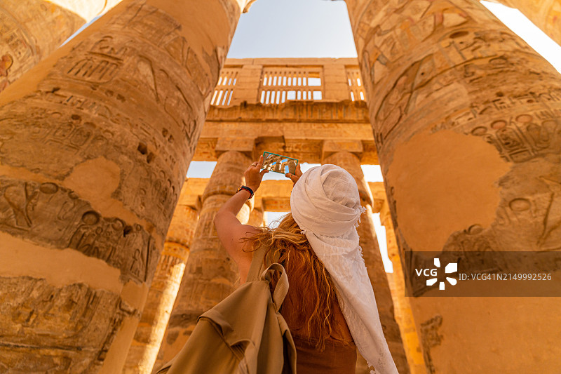 女游客走在卡纳克神庙大柱厅的柱子间，用智能手机拍照图片素材
