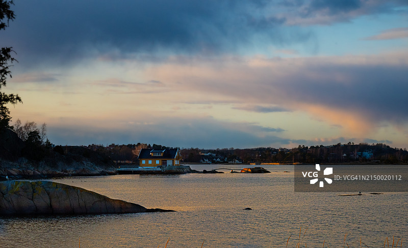 海岸线和黄色房屋的日落，两座桥梁通向海中岩石图片素材