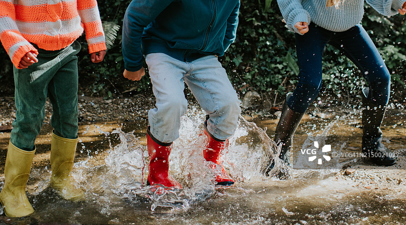 儿童穿着彩色雨靴在深水坑中跳跃特写图片素材