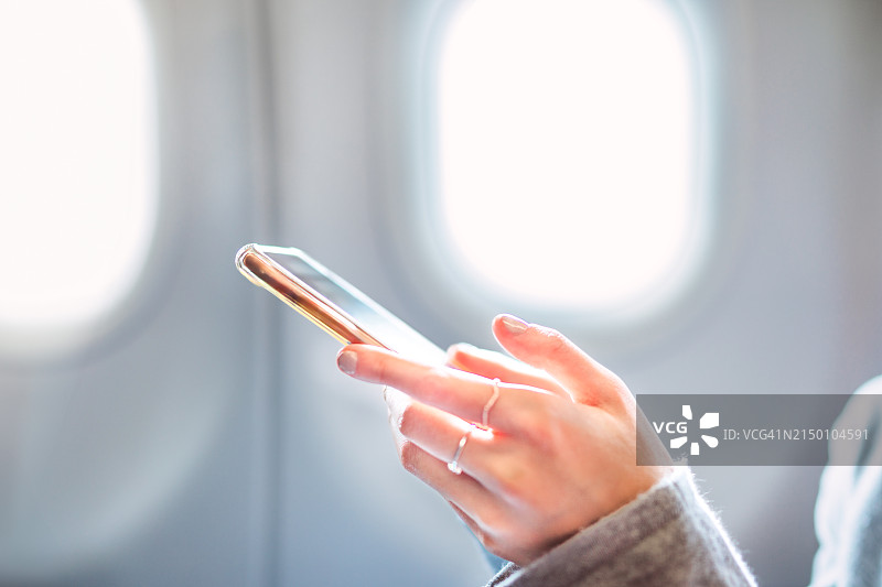 互联旅程：青少年女孩在飞机上使用智能手机的特写图片素材