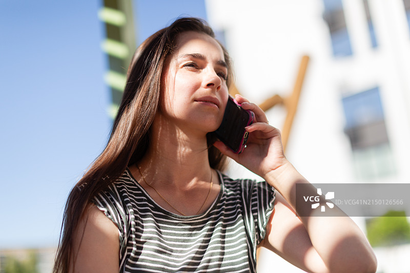 年轻女人在晴朗的户外打电话。图片素材