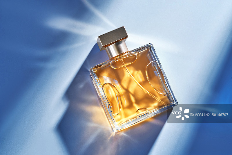 女士化妆品：玻璃瓶香水，蓝色背景下的光影效果图片素材