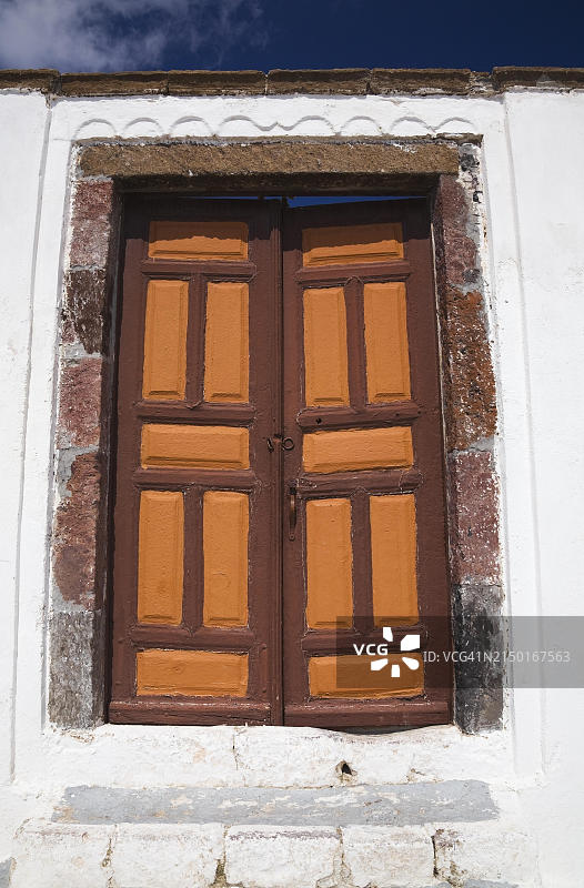 希腊圣托里尼费拉村白色粗糙外墙住宅上的棕橙色木制入口门图片素材