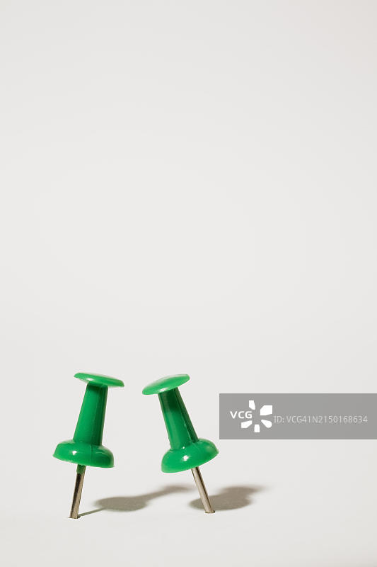 白色背景上两个直立的绿色塑料和铬制图钉特写，工作室构图，加拿大魁北克省，北美图片素材