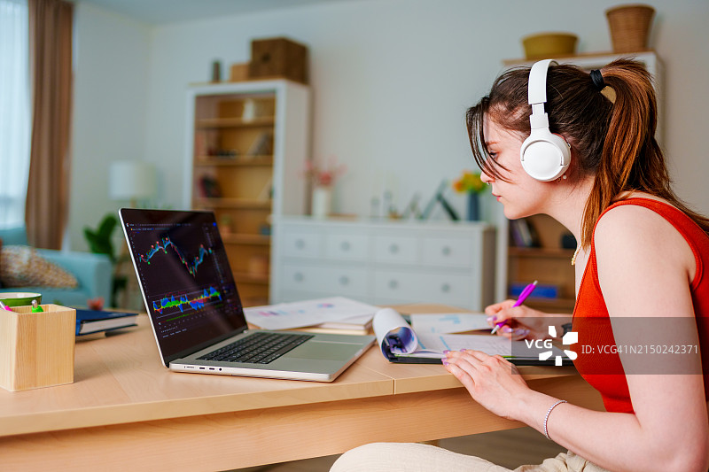 戴着耳机在笔记本电脑上查看比特币或股票交易所价格图表的年轻女商人图片素材
