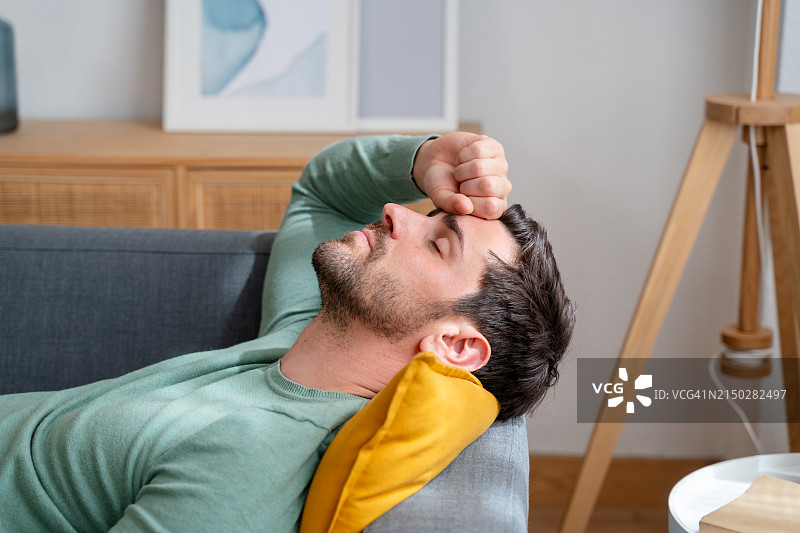 疲惫的年轻男子在家里的沙发上放松。图片素材