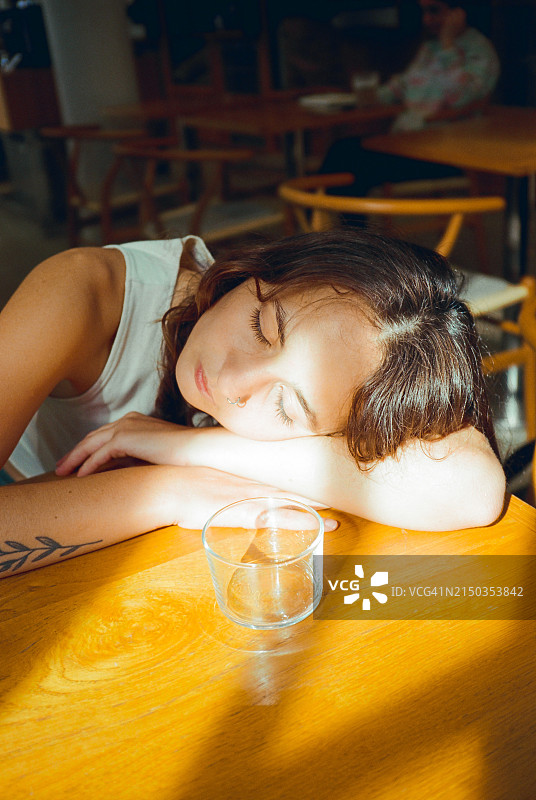 疲惫的女人享受阳光，将头靠在手臂上休息图片素材