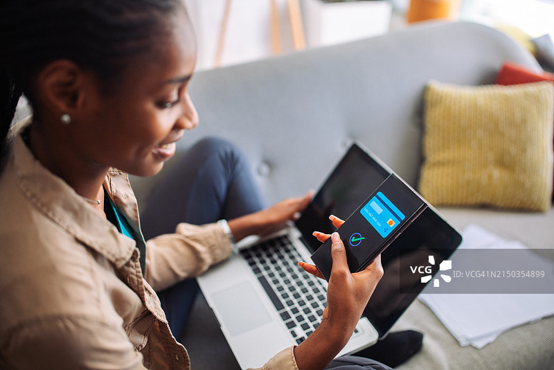 年轻的黑人女性在沙发上使用在线支付图片素材