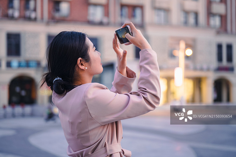 年轻女人用智能手机拍摄城市日落图片素材