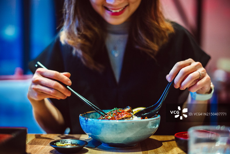 旅行餐饮体验：年轻亚洲女性在日式餐厅享用海鲜刺身饭图片素材