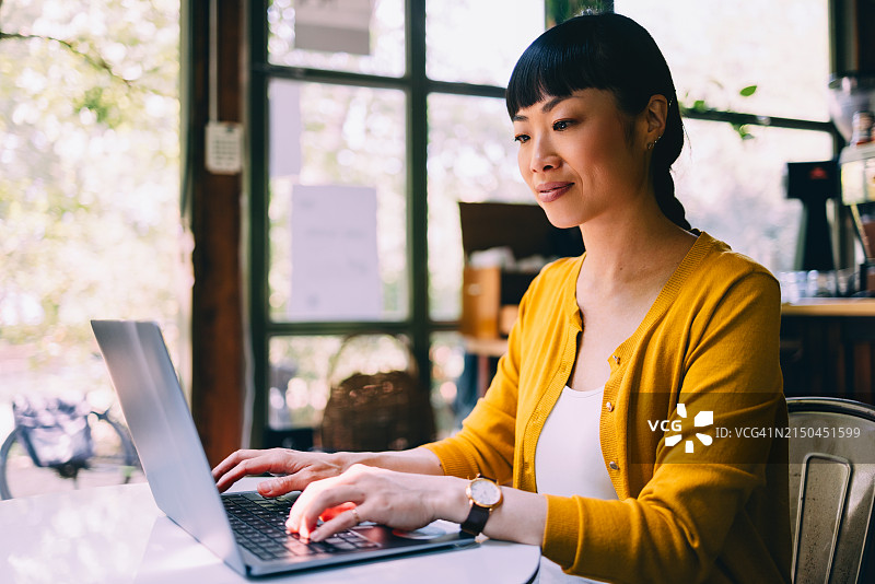 在咖啡馆用笔记本电脑愉快工作的亚洲女性图片素材