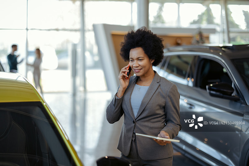 在汽车经销店用智能手机交谈的黑人女销售图片素材