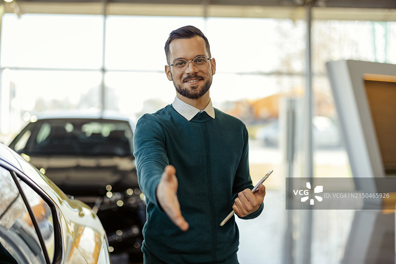 汽车展厅里，男销售员看着镜头伸出手准备握手图片素材