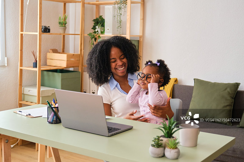 母亲工作时抱着正在玩眼镜的孩子图片素材