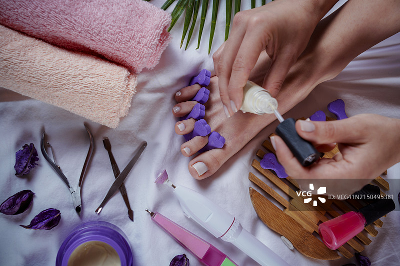 为有白色脚趾甲的女性进行足部护理，带有脚趾分离器图片素材