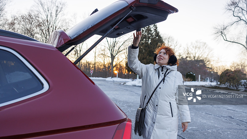 冬季驾车旅行：红发女子在阳光明媚的停车场关闭后备箱，准备出发图片素材