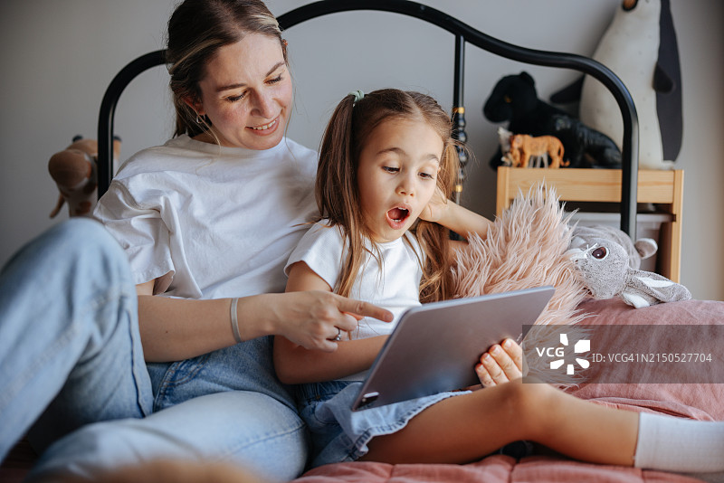 母女一起坐在床上看平板电脑图片素材