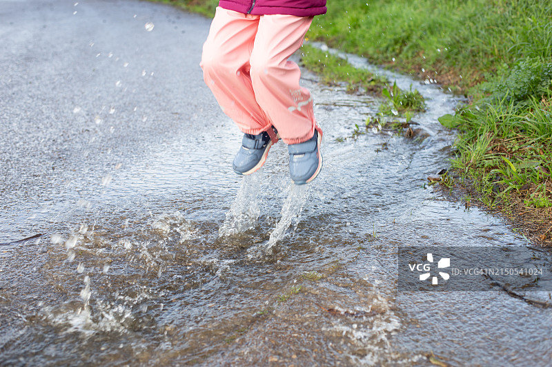 穿着雨衣的女孩在水坑里跳跃图片素材