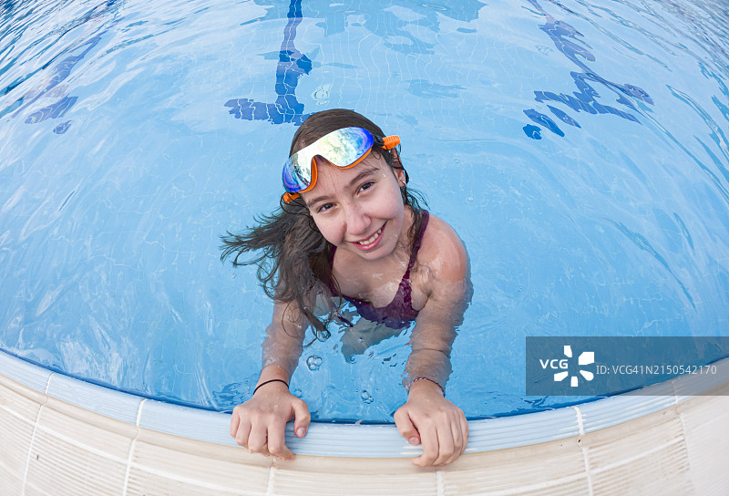 戴游泳镜的女孩在泳池边看向镜头图片素材