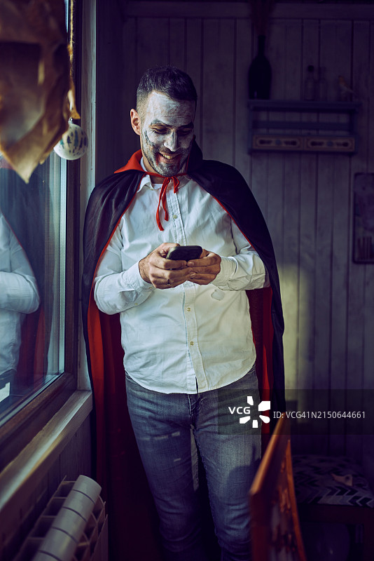 万圣节穿着吸血鬼服装使用手机的快乐男人。图片素材