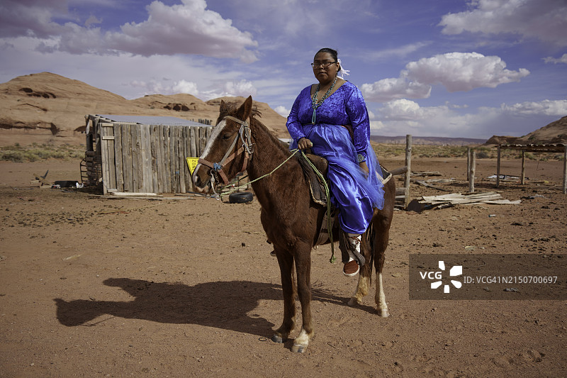 二十多岁的年轻纳瓦霍族妇女在纪念碑谷亚利桑那州给马戴上笼头，准备骑马图片素材