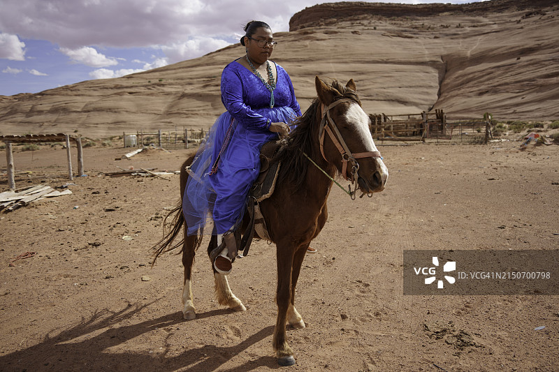 二十多岁的年轻纳瓦霍族妇女在纪念碑谷亚利桑那州给马戴上笼头，准备骑马图片素材