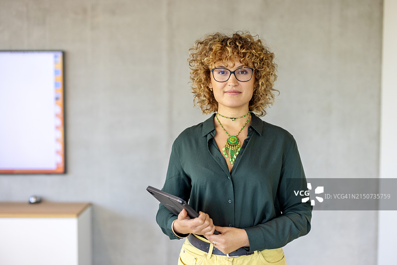 手持平板电脑站在办公室里的年轻漂亮女商人肖像图片素材