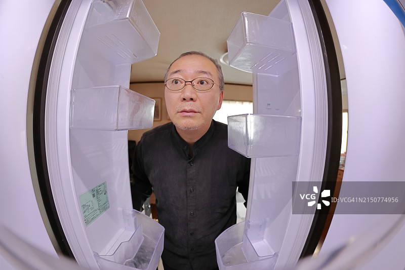 男人打开空冰箱的门，寻找食物和饮料图片素材