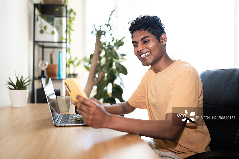 男人坐在办公桌前使用笔记本电脑和手机图片素材