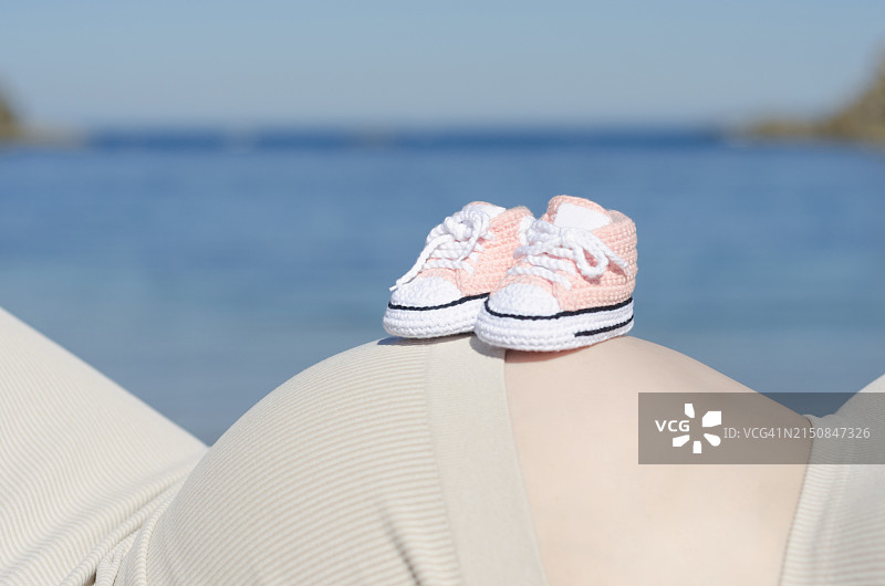 怀孕的宁静：孕妇腹部上的婴儿鞋图片素材